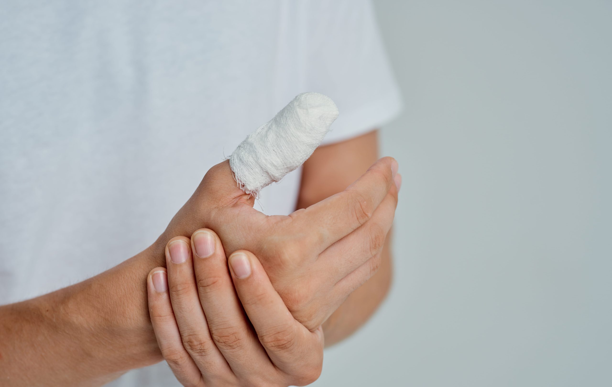 A close-up of a hand holding an injured thumb wrapped in a white medical bandage.