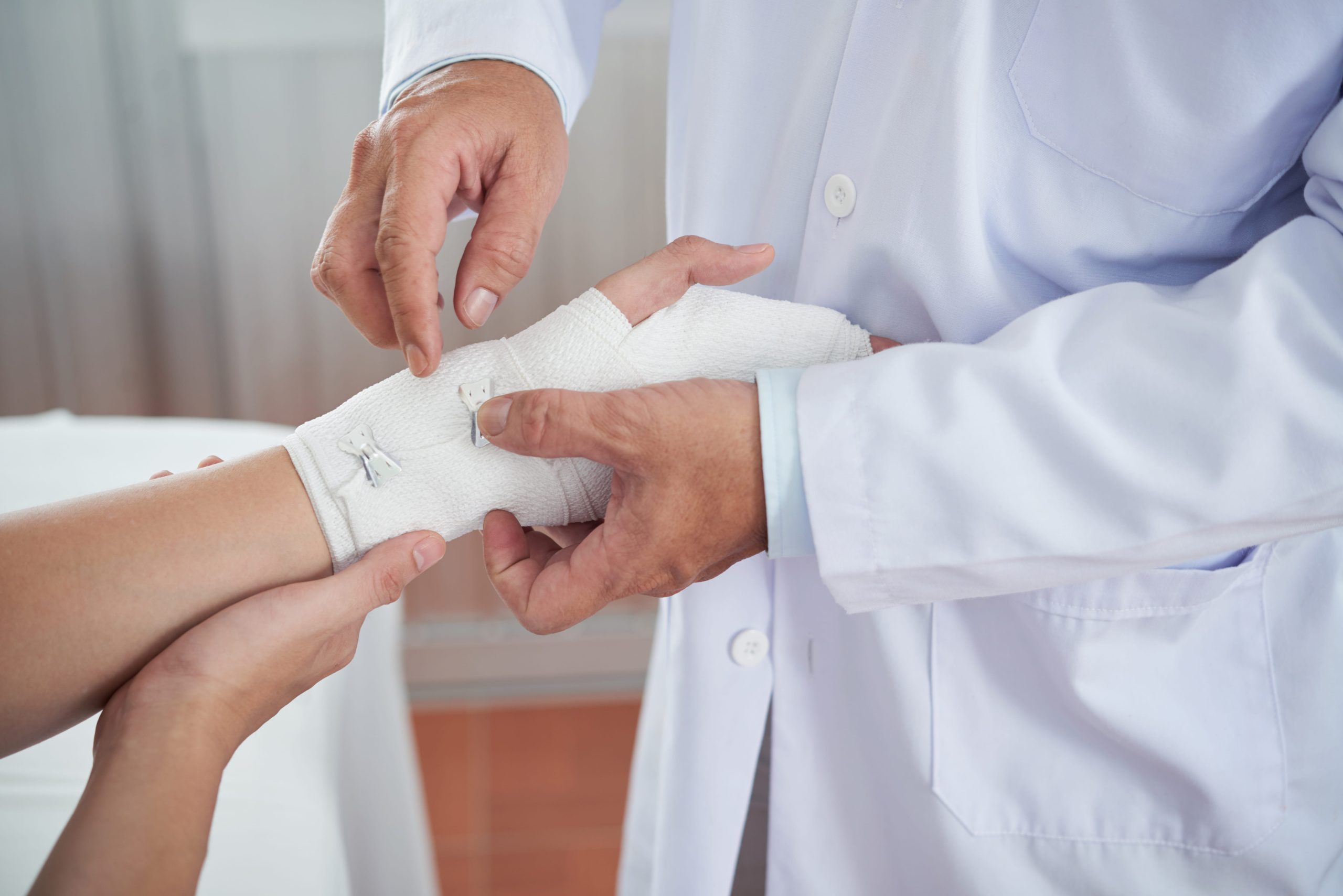 A doctor applying a bandage to a patient's hand in a medical setting.