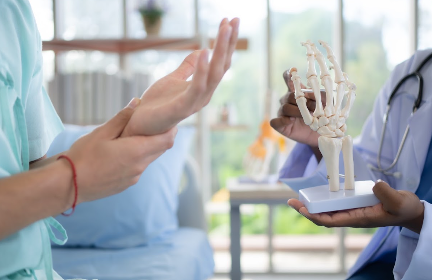 A doctor examining a patient's hand while demonstrating with a skeletal model of the hand.